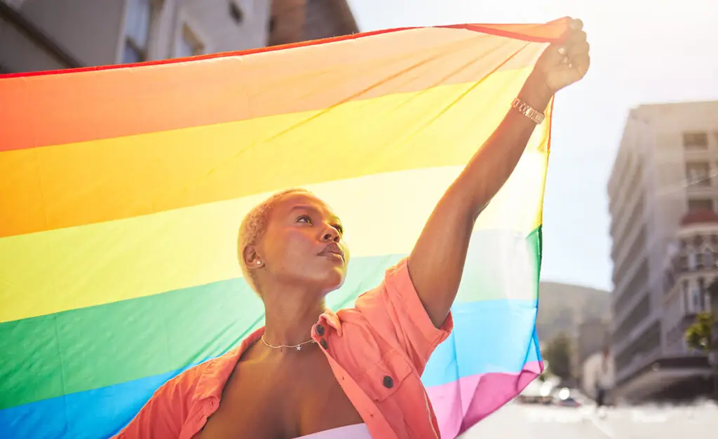 Lesbian, pride and black woman in city with flag for lgbtq community, ally or gay with support and equality in love outdoor. Rainbow, parade and lgbt awareness, inclusion and celebrate with sexuality