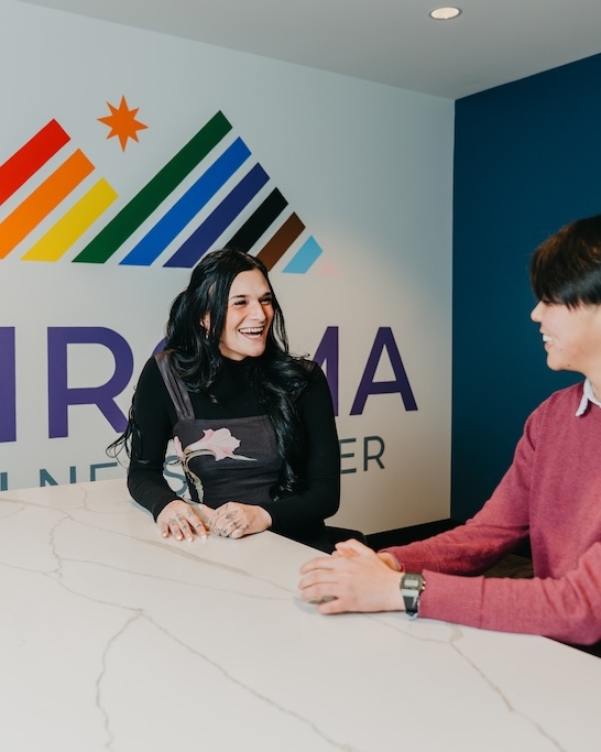 Two people talking and smiling at the front desk of Chroma Wellness Center, an LGBTQ+ affirming outpatient mental health treatment center in Denver.