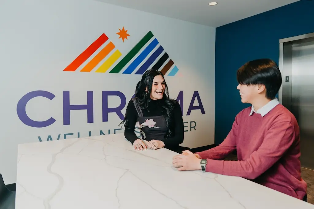 Two people talking and smiling at the front desk of Chroma Wellness Center, an LGBTQ+ affirming outpatient mental health treatment center in Denver.