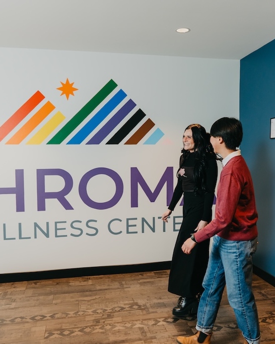 Two individuals walking through the lobby at Chroma Wellness Center, passing a colorful rainbow wall mural inside the LGBTQIA+ affirming mental health, trauma, and substance use treatment center.