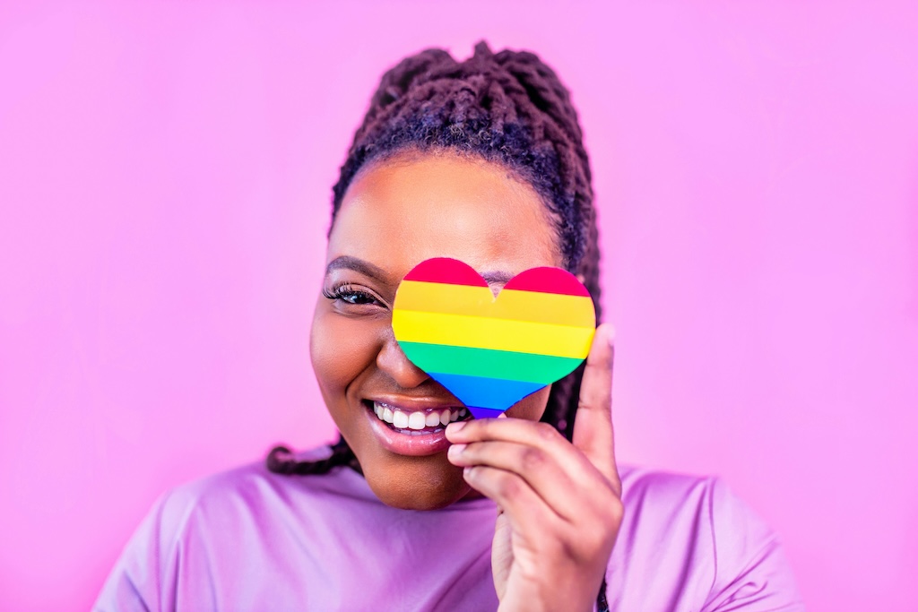Smiling individual holding a rainbow heart, representing inclusive and affirming mental health care at Chroma Wellness Center