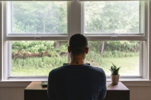 Person sitting at a desk looking out a window, representing reflection, mental health, and substance use recovery.