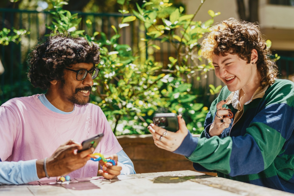 Two neurodivergent LGBTQIA+ people laughing together outdoors, representing neuroqueer identity, connection, and community.